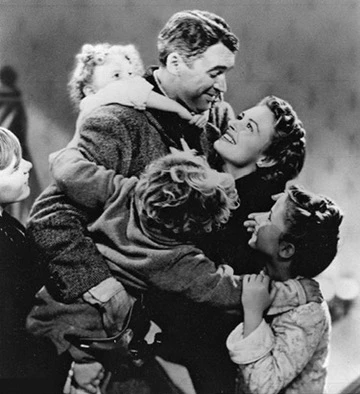 Black-and-white still from It’s a Wonderful Life: George and Mary Bailey hugging their children